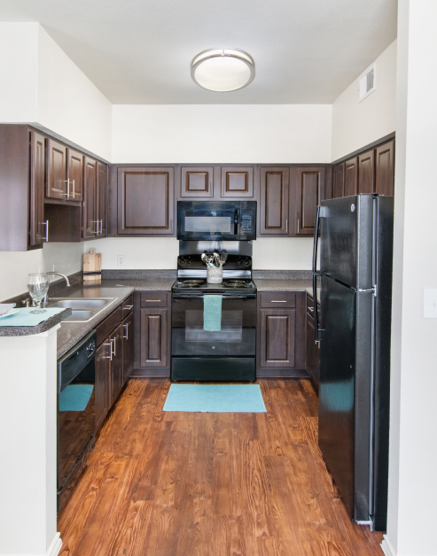 A modern kitchen featuring granite countertops, dark wood cabinets, modern appliances including refrigerator, oven, and dishwasher with wood flooring at MAA Watermark luxury apartments in Roanoke, TX