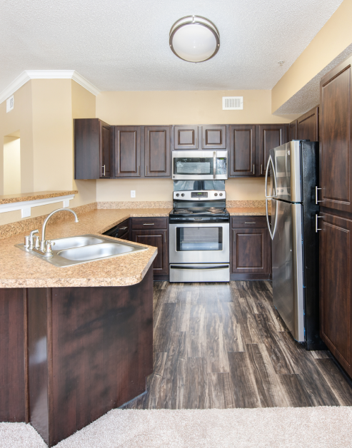 An upscale kitchen with dark wood cabinets and tan granite countertops, upgraded appliances and marble wood floors at MAA Willow Creek luxury apartments in Bedford, TX