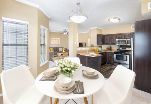 A small dining area with white round dining table and chairs under a hanging light fixture and bay windows with blinds at MAA Willow Creek luxury apartments in Bedford, TX