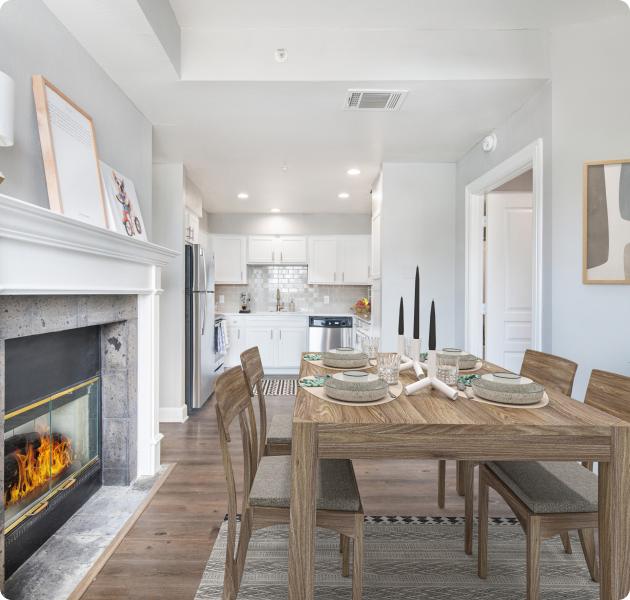 A luxurious apartment living room with a fireplace, dining table and chairs next to kitchen with sleek white cabinets and wood floors at MAA Worthington luxury apartments in Dallas, TX
