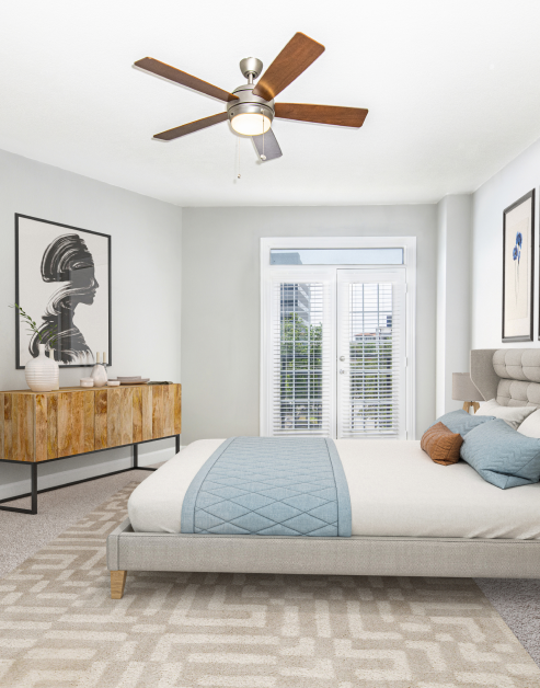 A modern bedroom featuring a wooden dresser next to French doors with white blinds and a ceiling fan at MAA Worthington luxury apartments in Dallas, TX