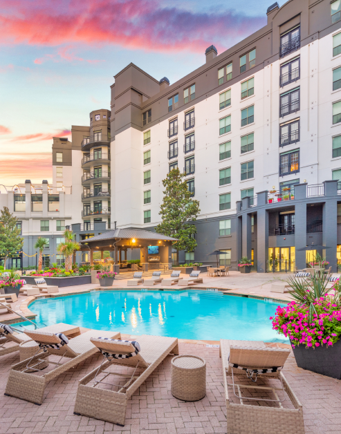 Luxurious swimming pool surrounded with lounge chairs with round side tables, pergola and potted flower planters at MAA Worthington luxury apartments in Dallas, TX