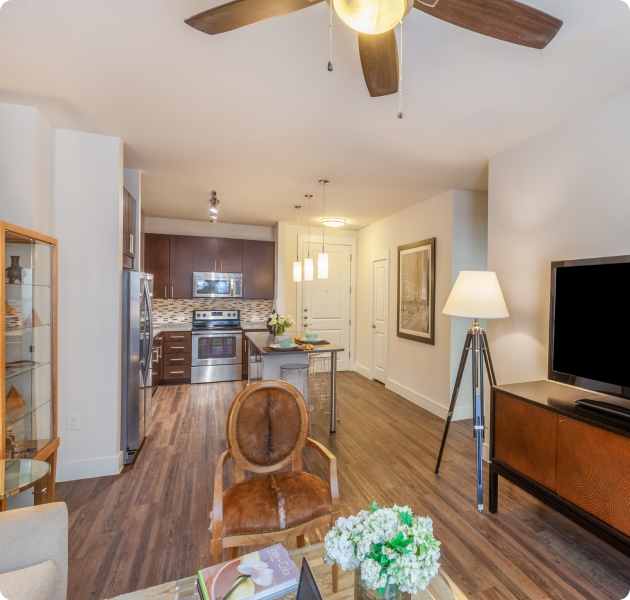 Apartment model living room area with TV on wood entertainment center with wood floors next to kitchen area at MAA 510 luxury apartments in Houston, TX
