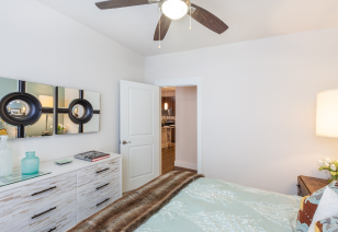 Model bedroom with ceiling fan and light-colored dresser with wall art next to doorway at MAA 510 luxury apartments in Houston, TX