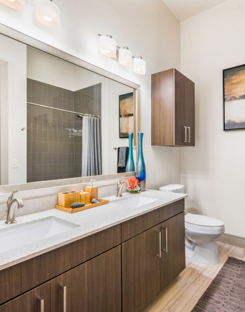 Modern bathroom with large vanity mirror on a white countertop with double sinks and wooden cabinets at MAA Afton Oaks luxury apartments in Houston, TX