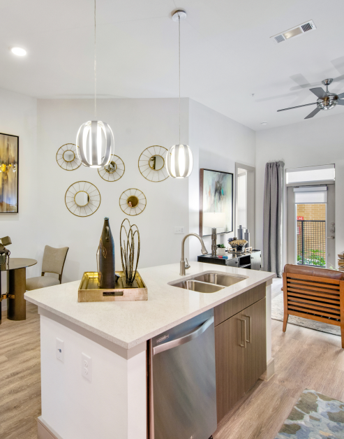 Stylish kitchen with hanging light fixtures and marble countertops next to dining area with stainless steel appliances and kitchen island on wood floors at MAA Afton Oaks luxury apartments in Houston, TX