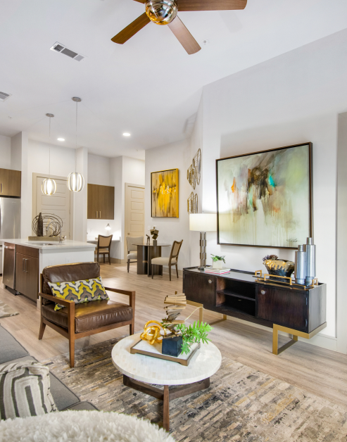 A model living room with a painting above a wooden cabinet, couch sitting area with marble top coffee table on an area rug with wood floors at MAA Afton Oaks luxury apartments in Houston, TX