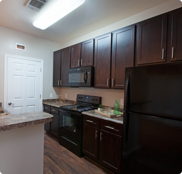 Stylish apartment kitchen with dark brown cabinets and upgraded appliances with wood floors and side door entrance at MAA Cypresswood luxury apartments in Spring, TX