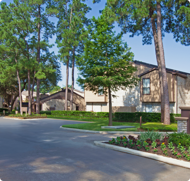 Community grounds with paved road surrounded by lush greenery and trees next to the apartment complex at MAA Cypresswood luxury apartments in Spring, TX