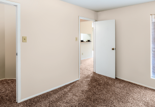 Corner view of carpeted bedroom with open doorway view of kitchen and living area at MAA Cypresswood luxury apartments in Spring, TX