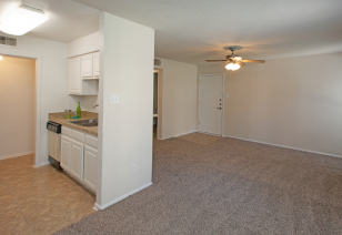 Corner view of empty carpeted living room with ceiling fan next to an open kitchen at MAA Cypresswood luxury apartments in Spring, TX