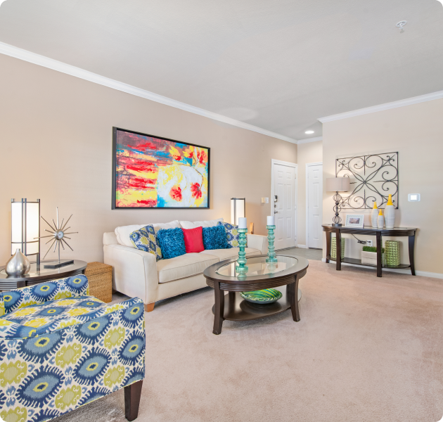 Apartment living room with colorful wall art above white couch, wood side table with decorative metal art and armchair and wood coffee table with glass top at MAA Energy Park luxury apartments in Houston, TX