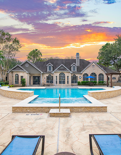 Center view of resort-style pool at sunset with a pergola and lounge chairs in front of the clubhouse at MAA Energy Park luxury apartments in Houston, TX