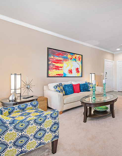 A spacious living room with a colorful wall painting above a white couch with ascent pillows, armchair and round wooden coffee table with a glass top at MAA Energy Park luxury apartments in Houston, TX