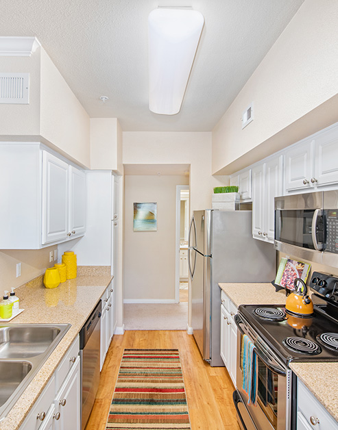 Modern-style wood floored kitchen with white cabinets, stainless steel appliances and light brown countertop with double sink at MAA Energy Park luxury apartments in Houston, TX