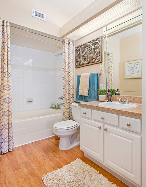 Bathroom with light brown countertop with sink, vanity mirror and white cabinets next to a bathtub with wood floors at MAA Energy Park luxury apartments in Houston, TX