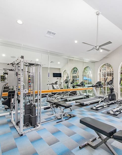 Modern fitness center with ceiling fan and vaulted ceiling and variety of workout equipment next to a  mirrored wall at MAA Energy Park luxury apartments in Houston, TX