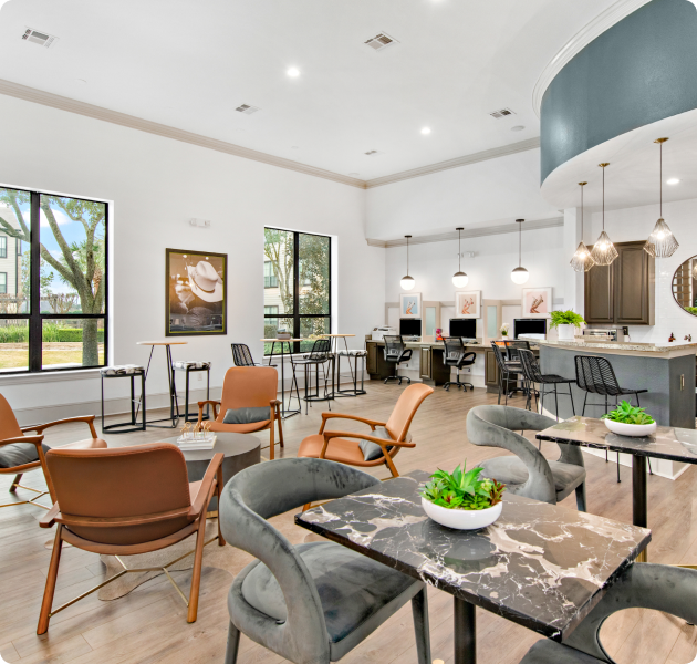 Community lounge area with coffee bar and business center with hanging lights, multiple seating areas on wood floors at MAA Fall Creek luxury apartments in Humble, TX