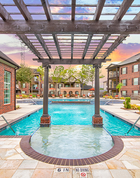 Resort-style pool with pool fountains and a pergola with lounge chairs at MAA Fall Creek luxury apartments in Humble, TX