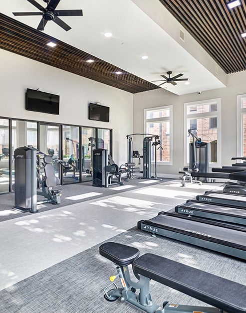 Upscale fitness center with stylish wood slats ceiling with fans, large windows and various exercise machines at MAA Grand Cypress luxury apartments in Cypress, TX