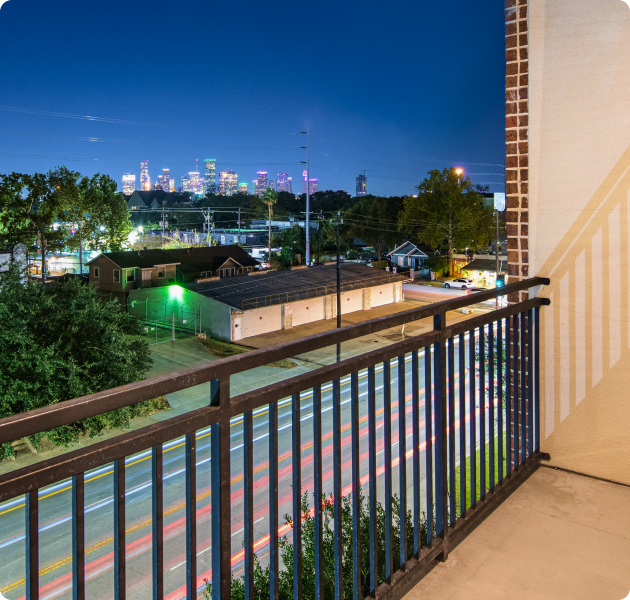 Private roadside apartment balcony with modern railings and a view of surrounding greenery and neighborhood streets at MAA Greater Heights luxury apartments in Houston, TX