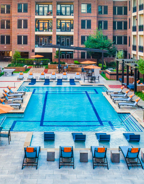 A resort-style pool with entrance steps and handrails surrounded by lounge chairs next to the apartment complex at MAA Greater Heights luxury apartments in Houston, TX