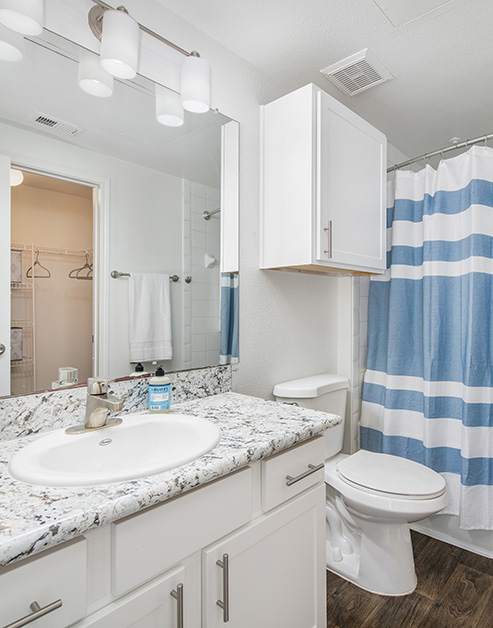 Modern bathroom with light fixtures above large vanity mirror with a sink, white cabinets and dark wood floors at MAA Kirkwood luxury apartments in Stafford, TX