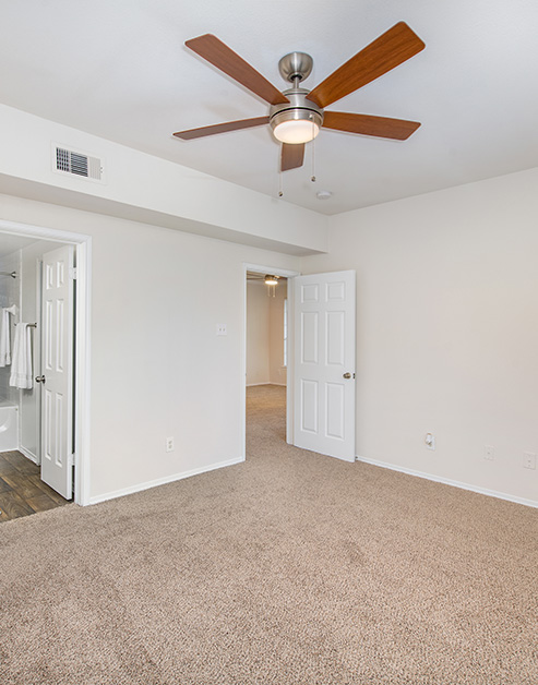 Empty master bedroom with a ceiling fan, carpeted floors and en-suite bathroom at MAA Kirkwood luxury apartments in Stafford, TX