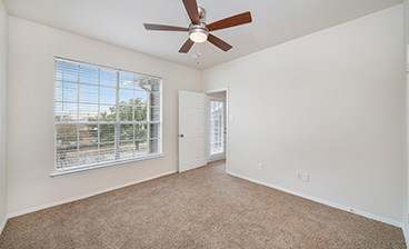 Corner view of carpeted bedroom with a ceiling fan and large picture window at MAA Kirkwood luxury apartments in Stafford, TX