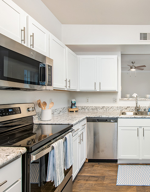 Modern-style kitchen with white cabinets, granite countertops with stainless-steel appliances and wood floors at MAA Kirkwood luxury apartments in Stafford, TX