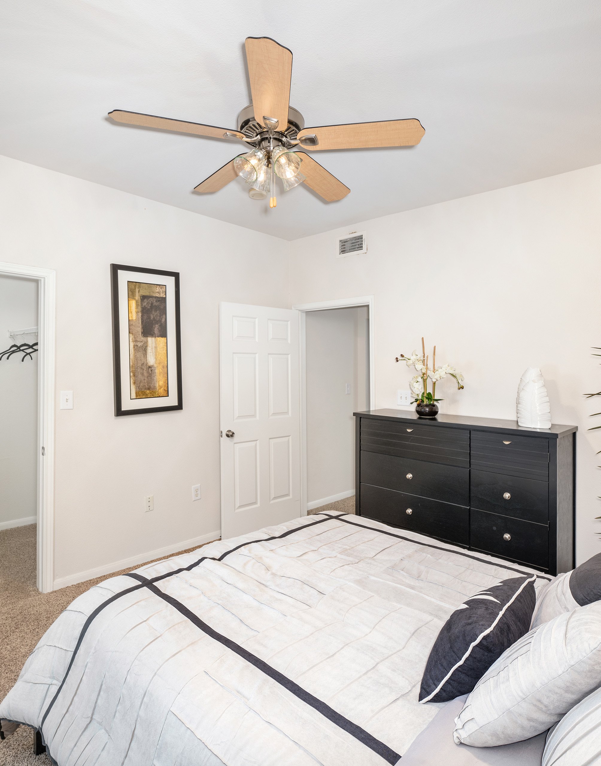Master bedroom with ceiling fan, white bed with accent pillows next to black dresser and a walk-in closet at MAA Legacy Pines luxury apartments in Houston, TX