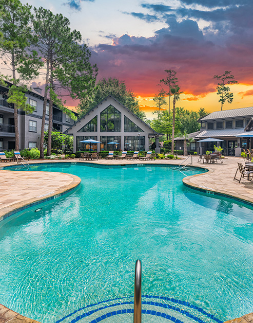 Resort-style pool with metal handle entrance surrounded by lounge chairs next to the clubhouse at MAA Legacy Pines luxury apartments in Houston, TX