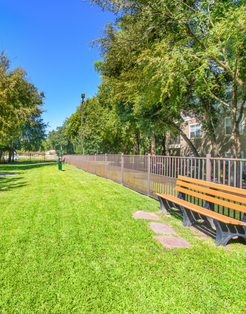 Gated dog park with grass and benches surrounded by lush trees at MAA Legacy Pines luxury apartments in Houston, TX