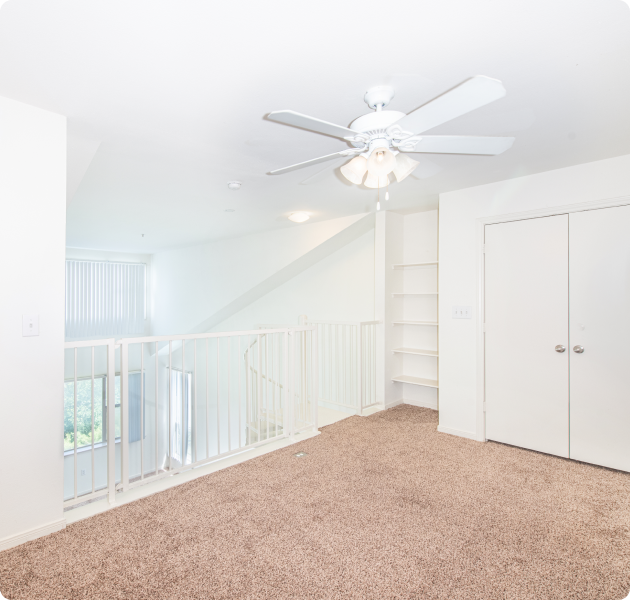 Apartment unit upstairs carpeted loft area with white ceiling fan and built-in shelving with close doors at MAA Midtown Square luxury apartments in Houston, TX