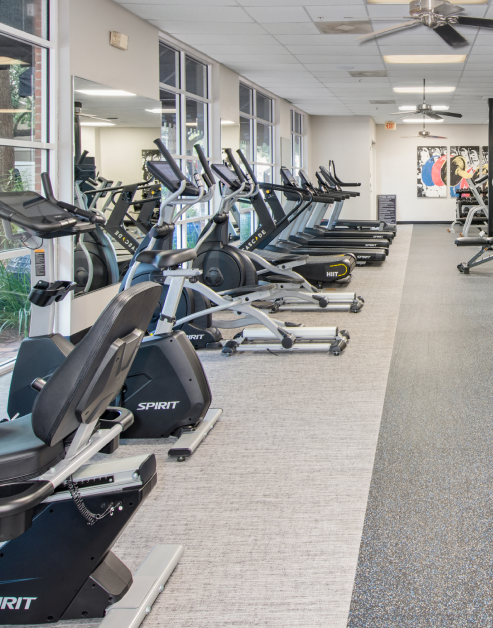 Community gym with row of elliptical and treadmill machines with ceiling fans at MAA Midtown Square luxury apartments in Houston, TX