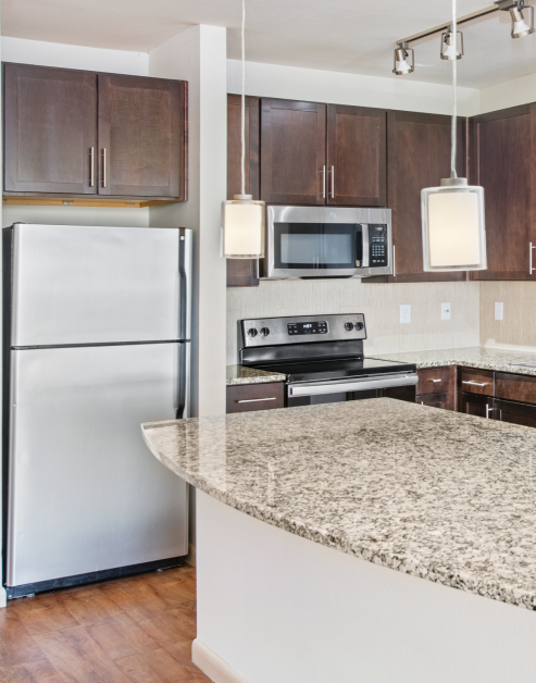 Modern kitchen with dark wood cabinets, stainless steel appliances, hanging lights and track lighting above kitchen island with granite countertops on wood floors at MAA Midtown Square luxury apartments in Houston, TX