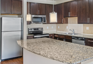 Kitchen with dark wood cabinets, stainless steel appliances, hanging lights above kitchen island with granite countertops MAA Midtown Square luxury apartments in Houston, TX