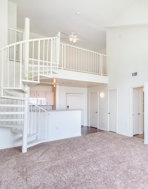 Spacious empty carpeted living room area with white spiral staircase to second floor loft area next to kitchen at MAA Midtown Square luxury apartments in Houston, TX