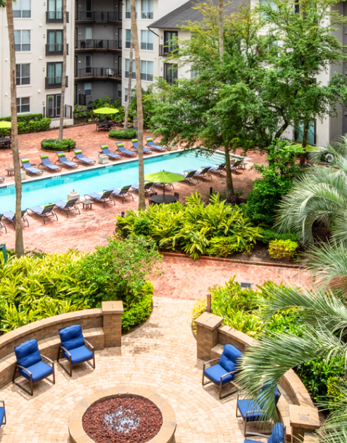 Swimming pool surrounded by lounge chairs and tables and chairs next to firepit with sitting area and lush greenery at MAA Midtown Square luxury apartments in Houston, TX