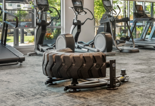 Close up view of fitness center tire flip machine next to treadmills and ellipticals and large picture windows at MAA Park Point luxury apartments in Houston, TX