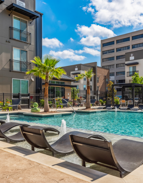 Resort-style pool with a sundeck and water fountains, surrounded by lounge chairs and palm trees situated next to the apartment complex at MAA Park Point luxury apartments in Houston, TX