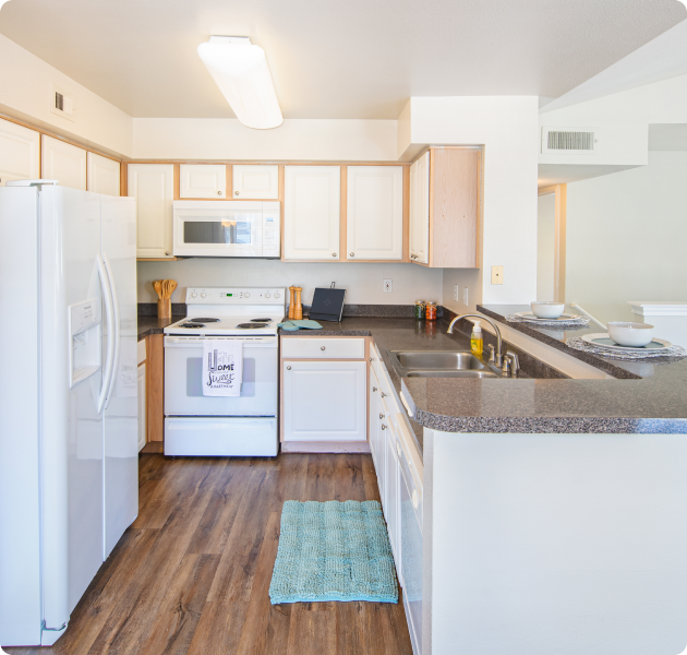 Apartment kitchen with bar top counter, double sink and white appliances and cabinets on wood floors at MAA Ranchstone luxury apartments in Houston, TX