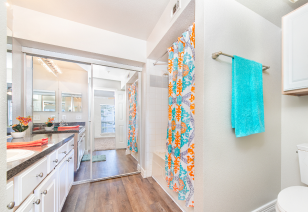 Bathroom with mirrored sliding closet doors, countertop with sink and white cabinets next to colorful shower curtains on wood floors at MAA Ranchstone luxury apartments in Houston, TX