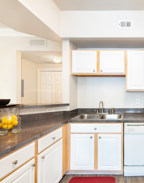 Kitchen with bar top counter, a sink on dark counter tops with white cabinets and wood floors at MAA Ranchstone luxury apartments in Houston, TX