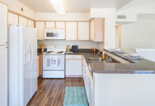 Long view of an open kitchen with bar top counter, white appliances and cabinets on wood floors at MAA Ranchstone luxury apartments in Houston, TX