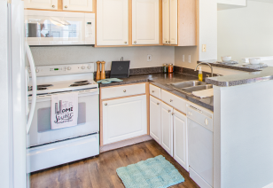 Corner view of a kitchen with oven, a double sink with dark countertops and white cabinets on wood floors at MAA Ranchstone luxury apartments in Houston, TX