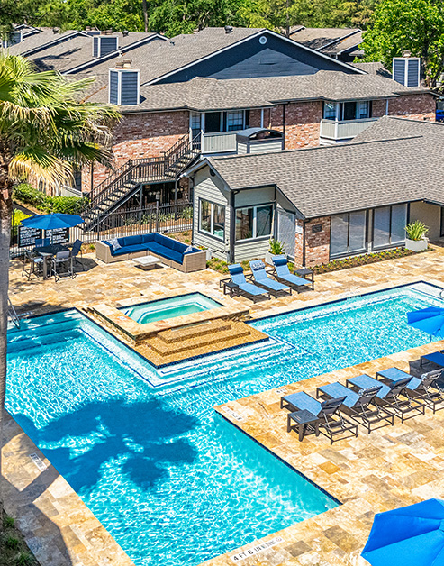 Long view of resort-style swimming pool with sundeck, entrance steps and lounge chairs situated next to the apartment complex at MAA Valleywood luxury apartments in the Woodlands, TX