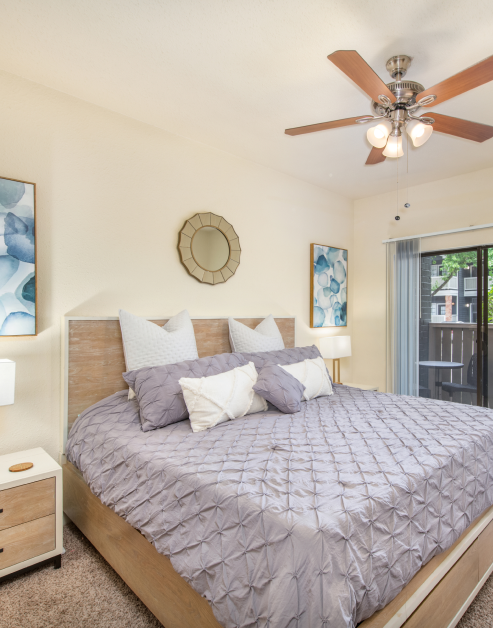 Carpeted bedroom with sliding glass doors and a ceiling fan with wall art over the bed and nightstands at MAA Valleywood luxury apartments in the Woodlands, TX