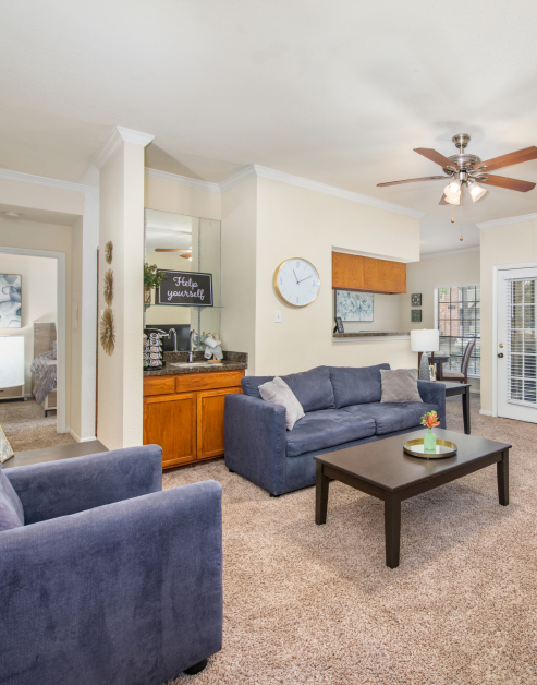 Carpeted living room with ceiling fan, coffee bar with cabinets, blue couch and arm chair with wood coffee table at MAA Valleywood luxury apartments in the Woodlands, TX