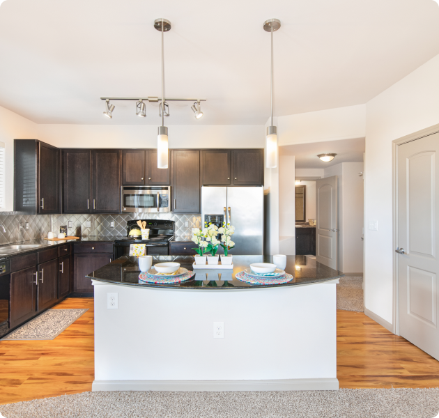 Modern-style apartment kitchen with stainless-steel appliances, dark brown cabinets with tile backsplash and kitchen island on wood floors at MAA Vintage Park luxury apartments in Houston, TX